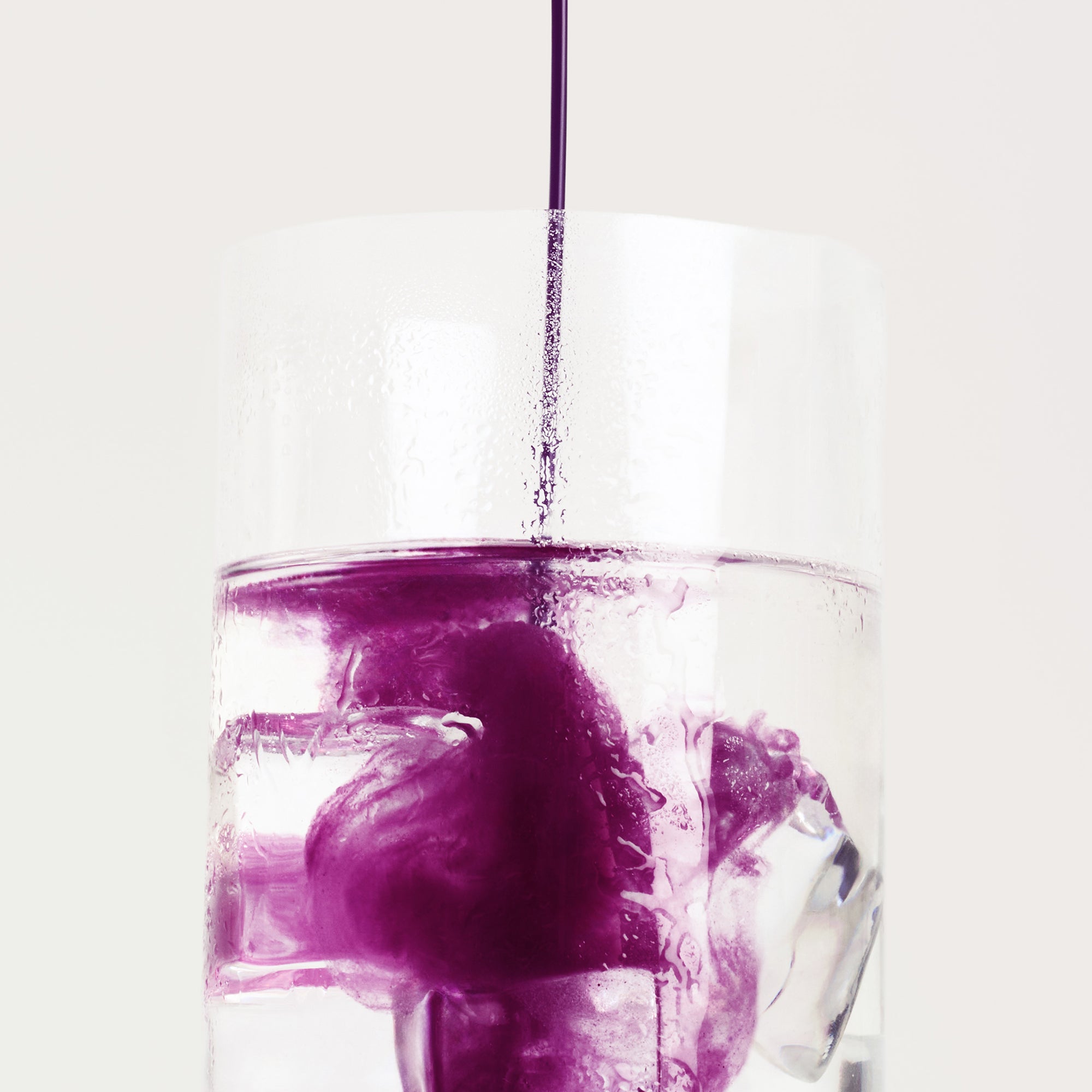 Dissolution instantanée de la poudre de ube Seven Taste dans un verre d'eau de coco froide avec glaçons, couleur violette vibrante naturelle